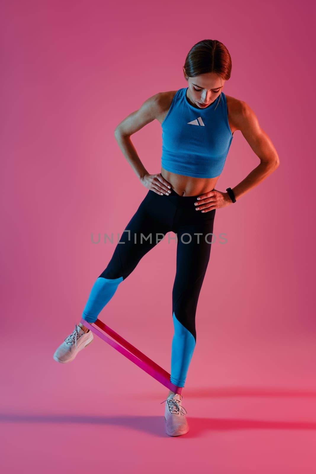 Athletic active woman standing and stretching elastic band with legs on studio background by Yaroslav_astakhov