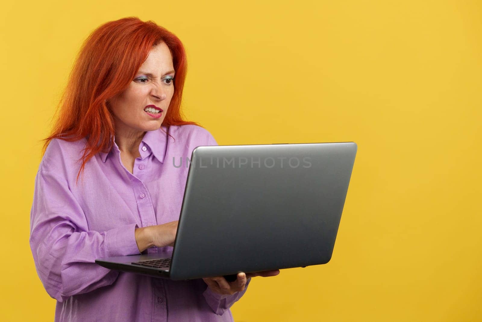 Mature redheaded woman having a problem with a laptop in studio with yellow background