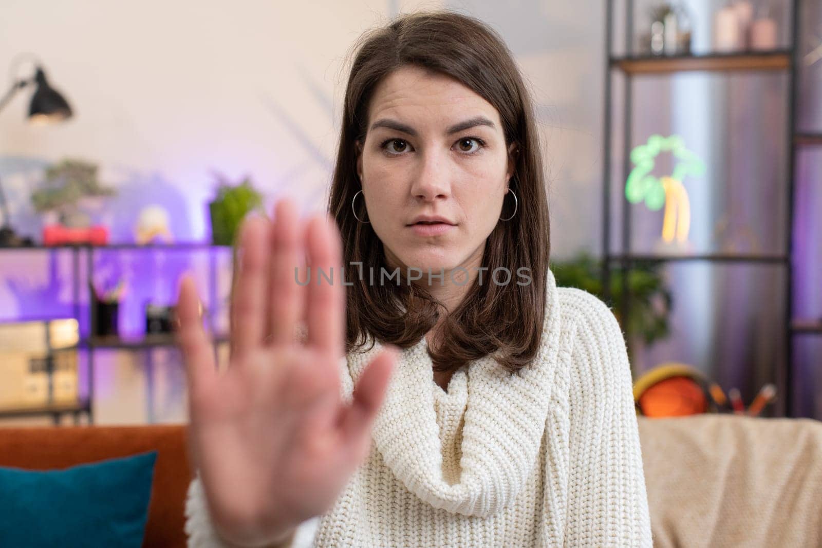 Stop gesture. Angry young woman say No hold palm folded crossed hands, warning of finish, prohibited access, declining communication, body language, danger at home room. Pretty girl sitting on couch