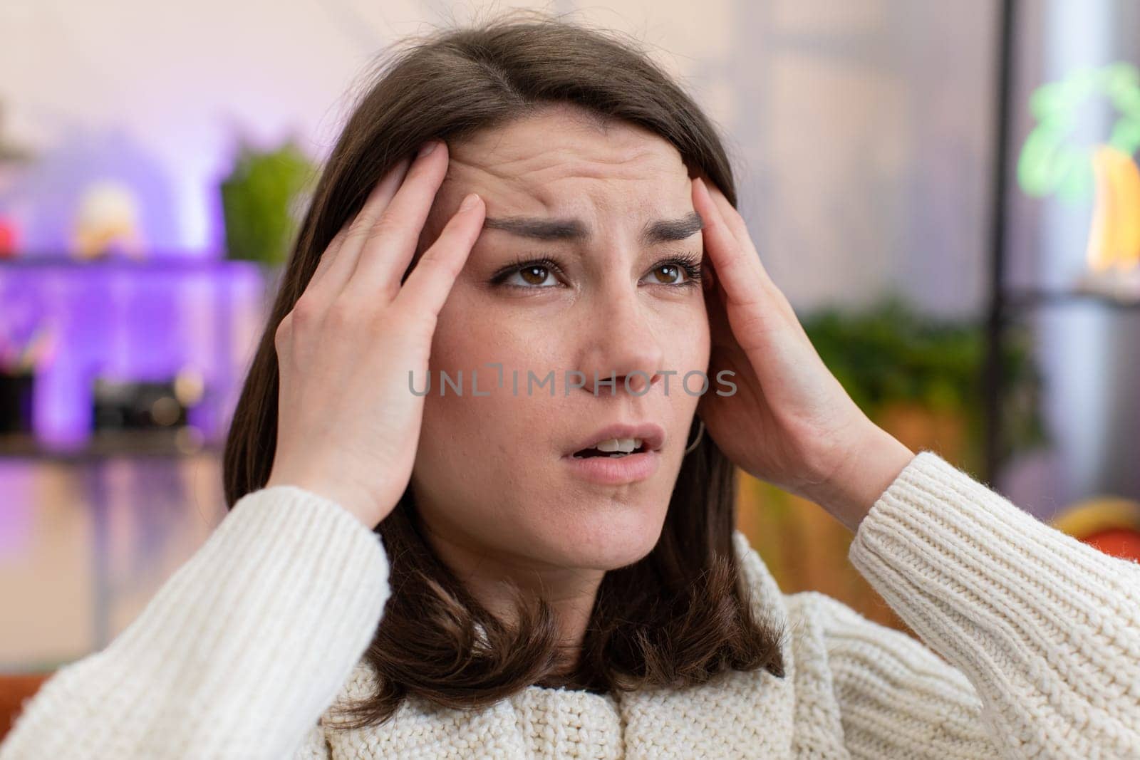 Displeased young woman rubbing temples to cure headache problem, suffering from tension and migraine, stress grimacing in pain high blood pressure at home room apartment. Girl on couch. Lifestyles