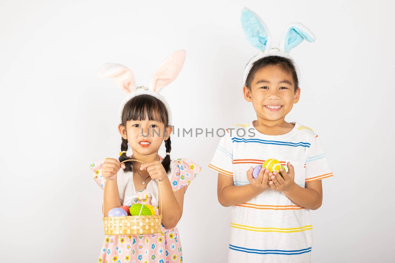 Happy Easter Day. Two smile Asian little girl and boy wearing easter bunny ears holding basket with eggs isolated on white background with copy space, Happy family children in holiday