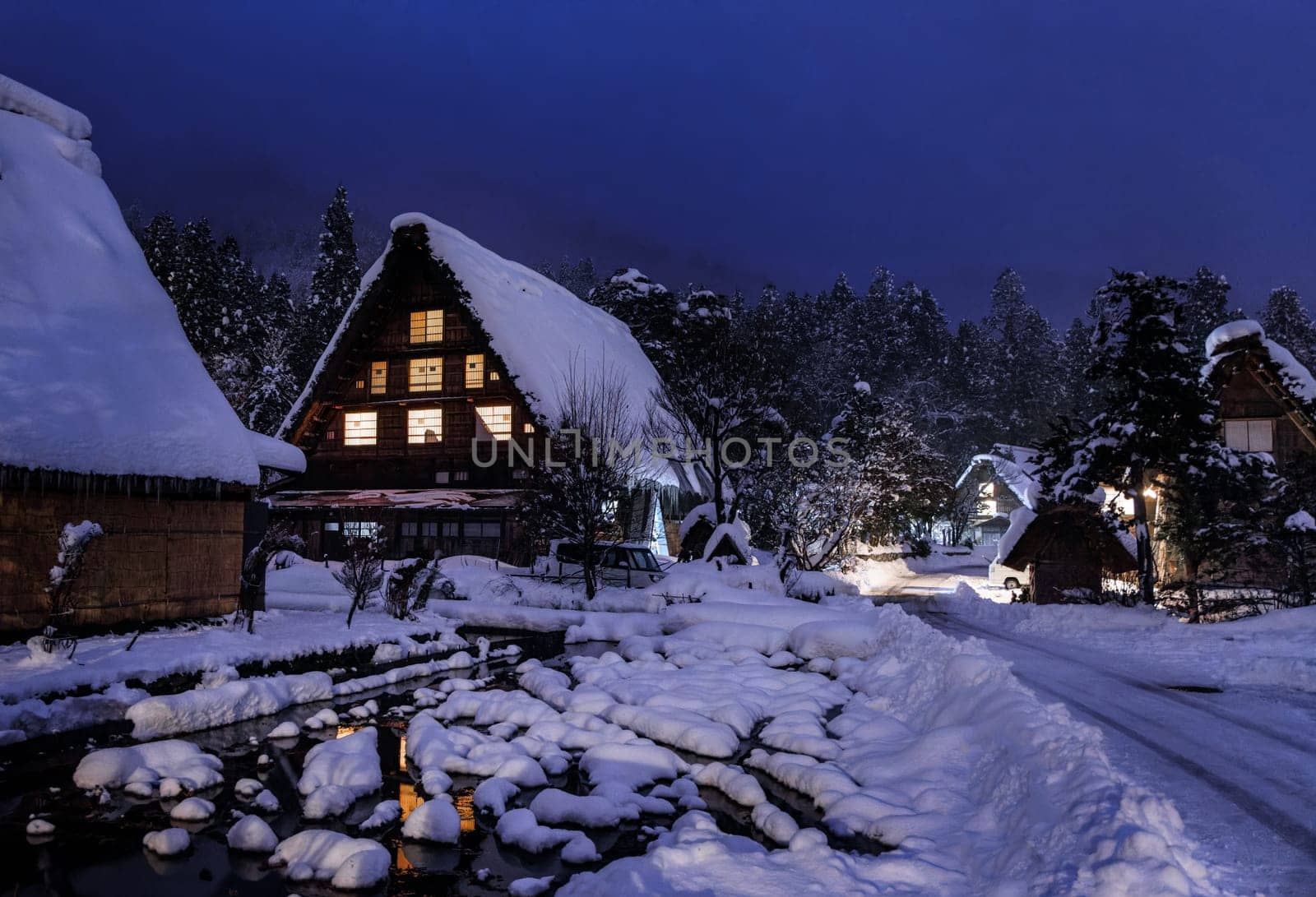 Snow covered Japanese farmhouse in historic village by woods at night by Osaze