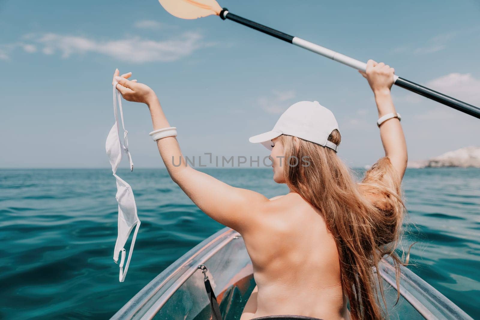 Woman in kayak back view. Happy young woman with long hair floating in transparent kayak on the crystal clear sea. Summer holiday vacation and cheerful female people having fun on the boat.