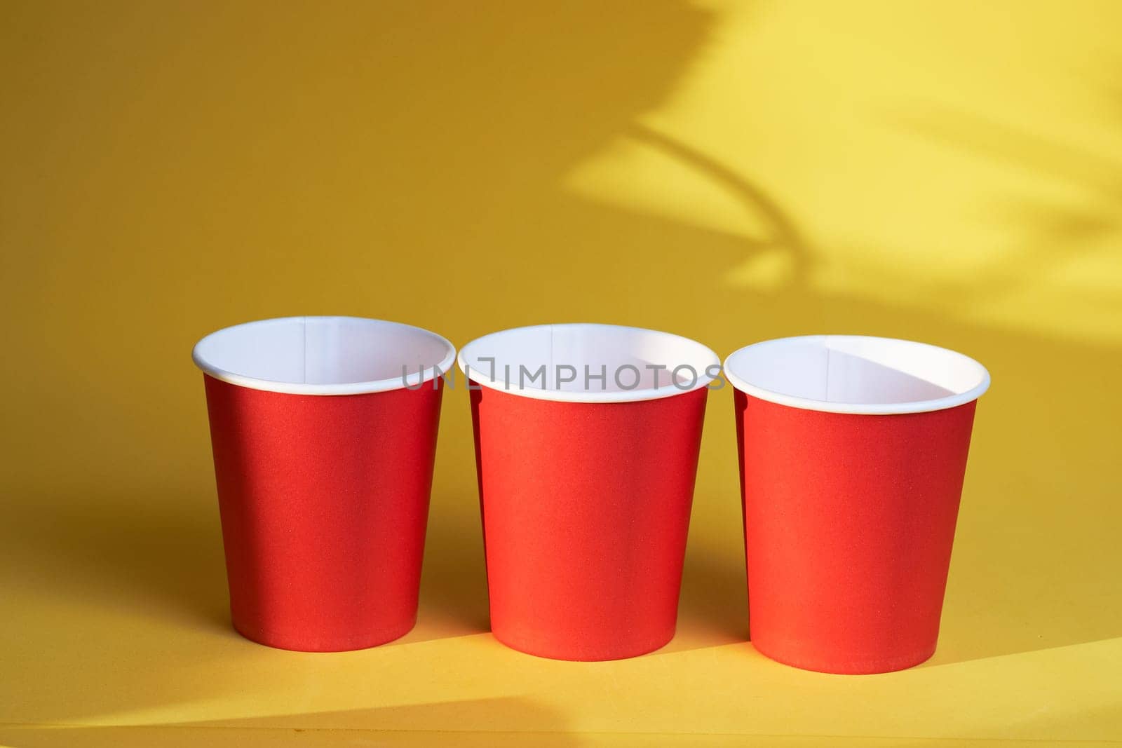 Three bright red disposable cups on a yellow background by Севостьянов