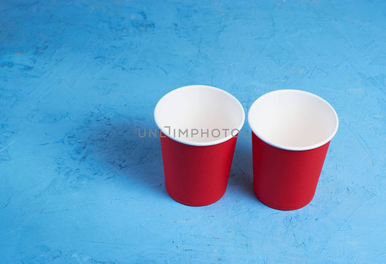 Two red paper coffee cups on a blue background. Morning concept.