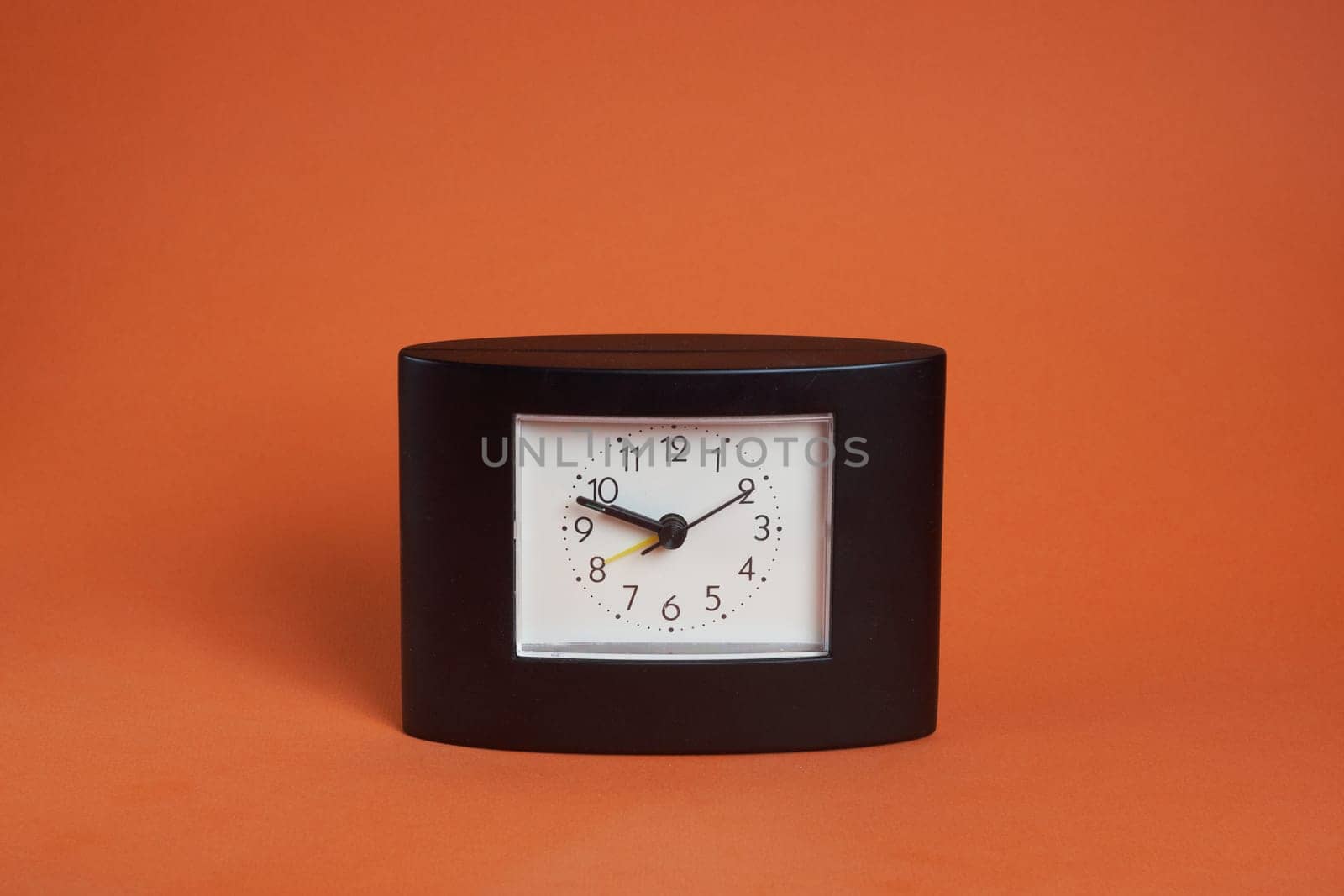 A square-shaped black desk clock with a white dial on a brown background and a place to copy text.