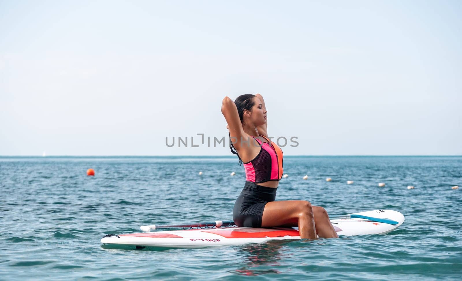 Silhouette of woman standing, surfing on SUP board, confident paddling through water surface. Idyllic sunset or sunrise. Sports active lifestyle at sea or river.