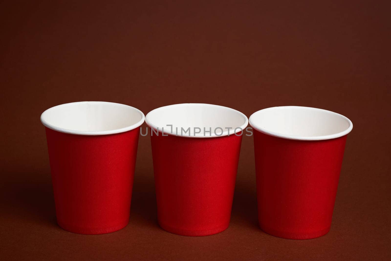Three red disposable cups on a dark brown background. by Севостьянов