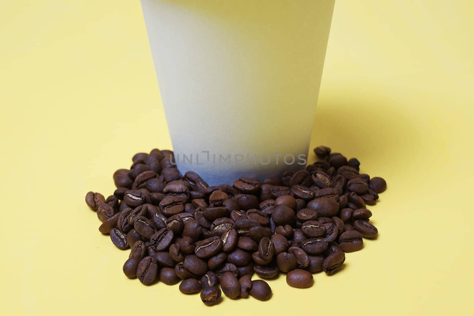 coffee beans next to a paper cup with coffee beans, white,yellow background