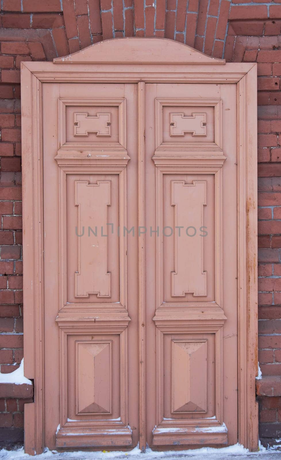 An old brown double-leaf wooden door on a brick wall