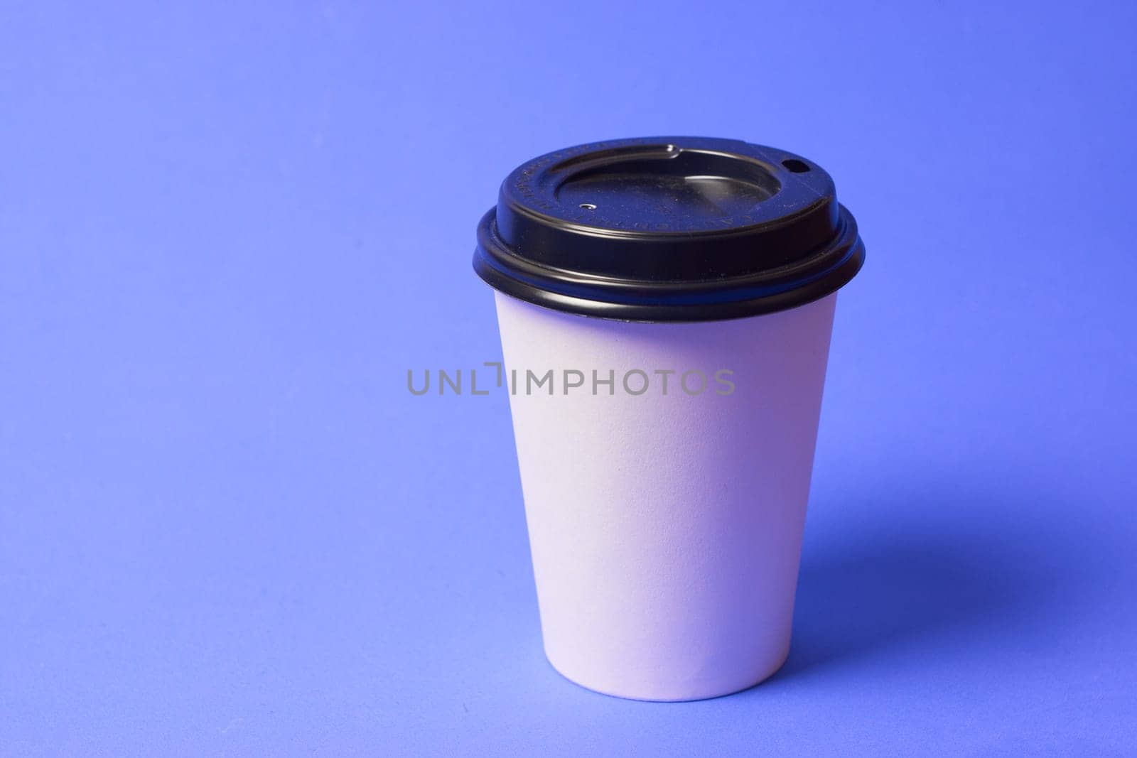 Paper coffee container with a black lid and on a blue background a white coffee paper cup with a black lid takeaway coffee