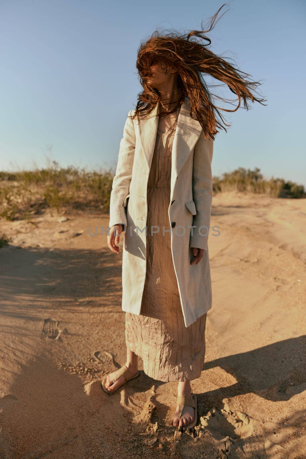 a stylish woman in fashionable summer clothes stands in the sand against a blue sky with her face covered by her hair. High quality photo