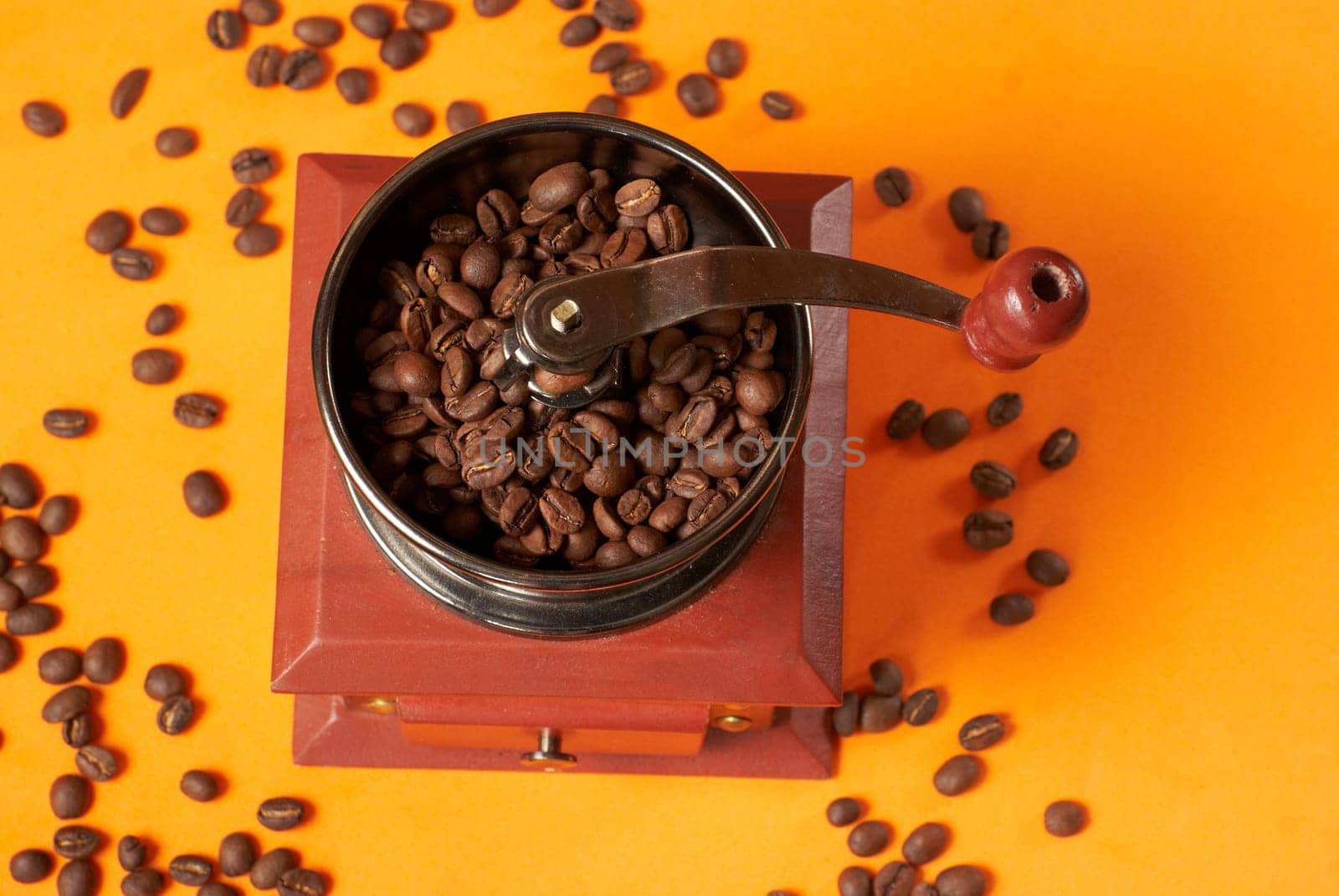 Manual coffee grinder for grinding coffee beans. On an orange background with coffee beans