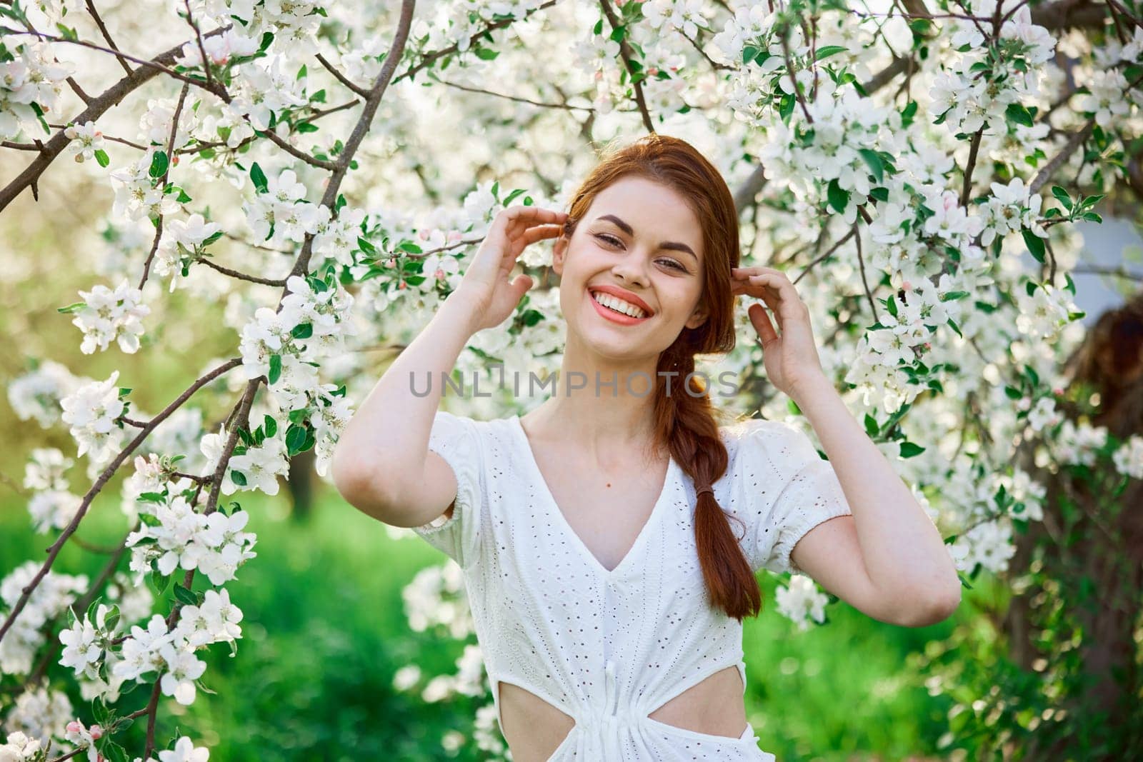 portrait of a happy, laughing red-haired woman next to a flowering tree in the garden by Vichizh