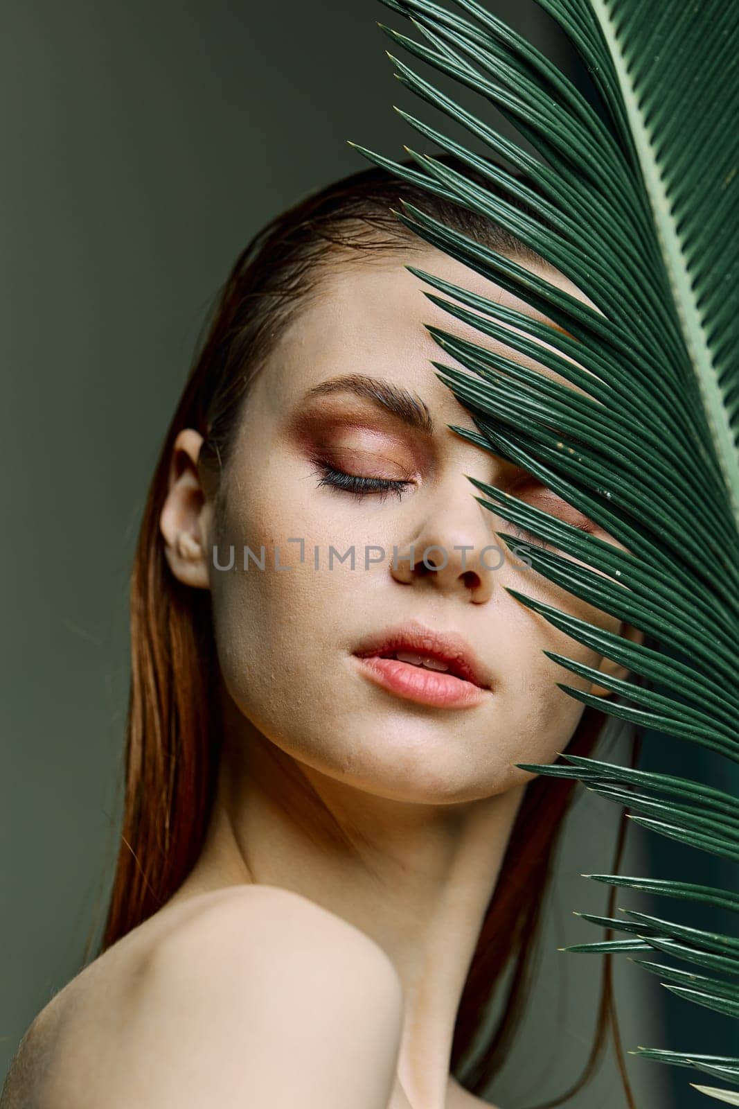 a close beauty portrait of a beautiful woman standing holding a palm leaf near her face, closing her eyes. Vertical photo without retouching of problem skin by Vichizh