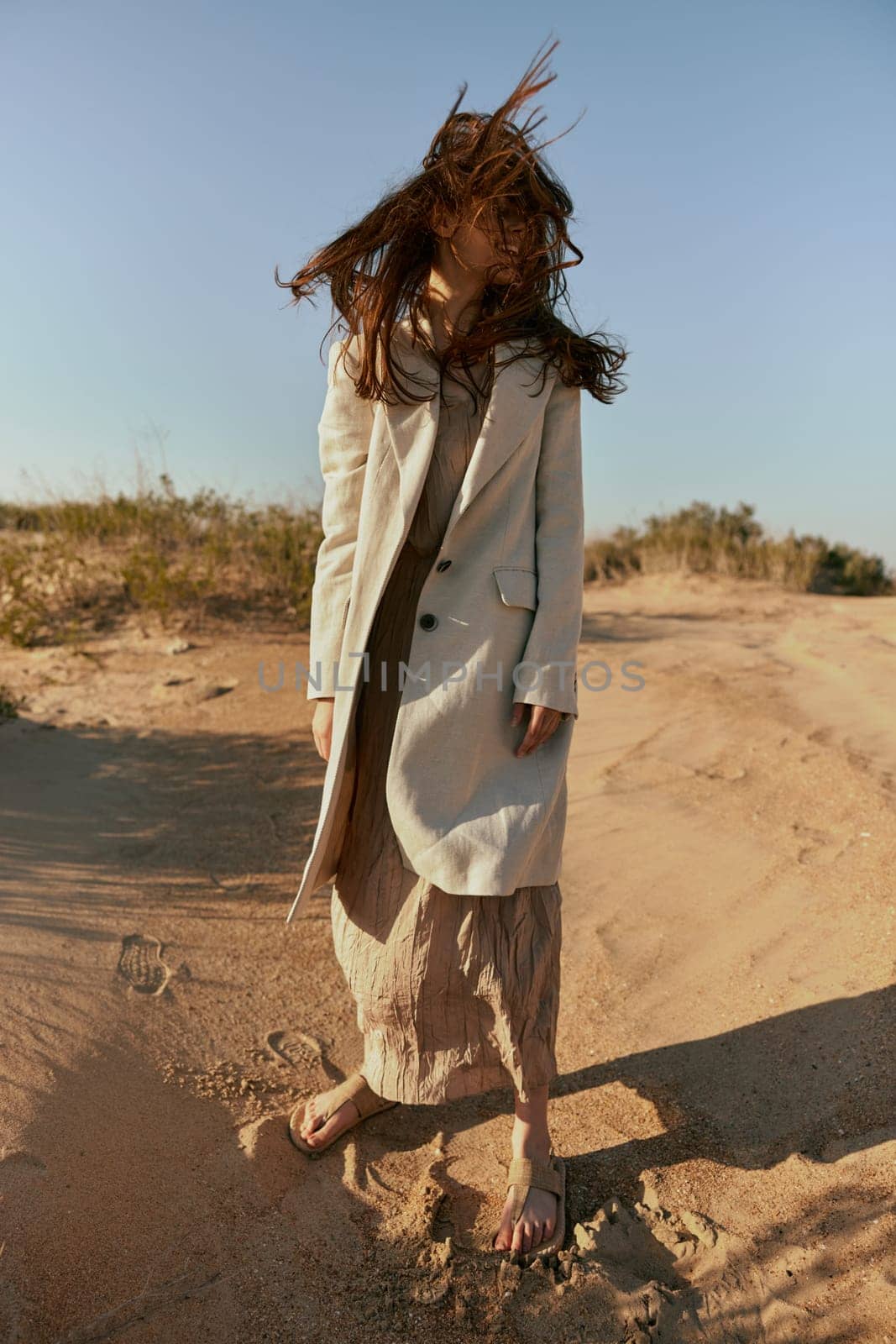 an atypical portrait of a woman in stylish summer clothes stands on the sands with hair covering her face. High quality photo