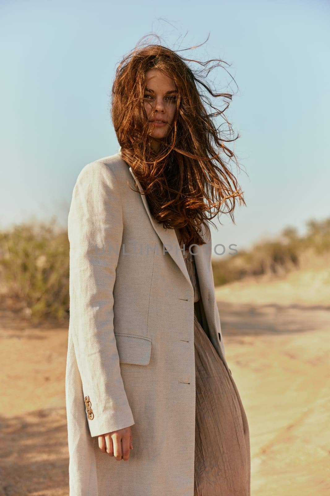 a beautiful woman in a light jacket looks at the camera while standing in nature and the wind blows her hair. High quality photo