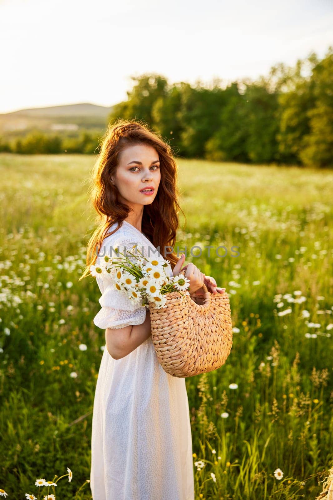 close portrait of a happy woman looking at the camera in a light dress and a wicker basket in her hands with chamomile flowers in nature by Vichizh