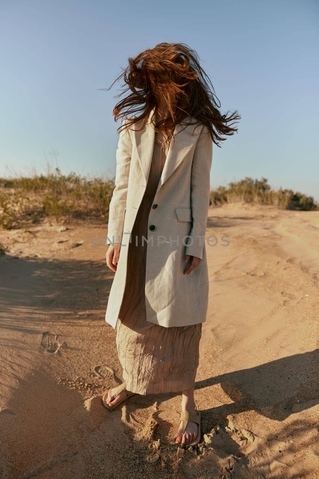 an atypical portrait of a woman in stylish summer clothes stands on the sands with hair covering her face. High quality photo