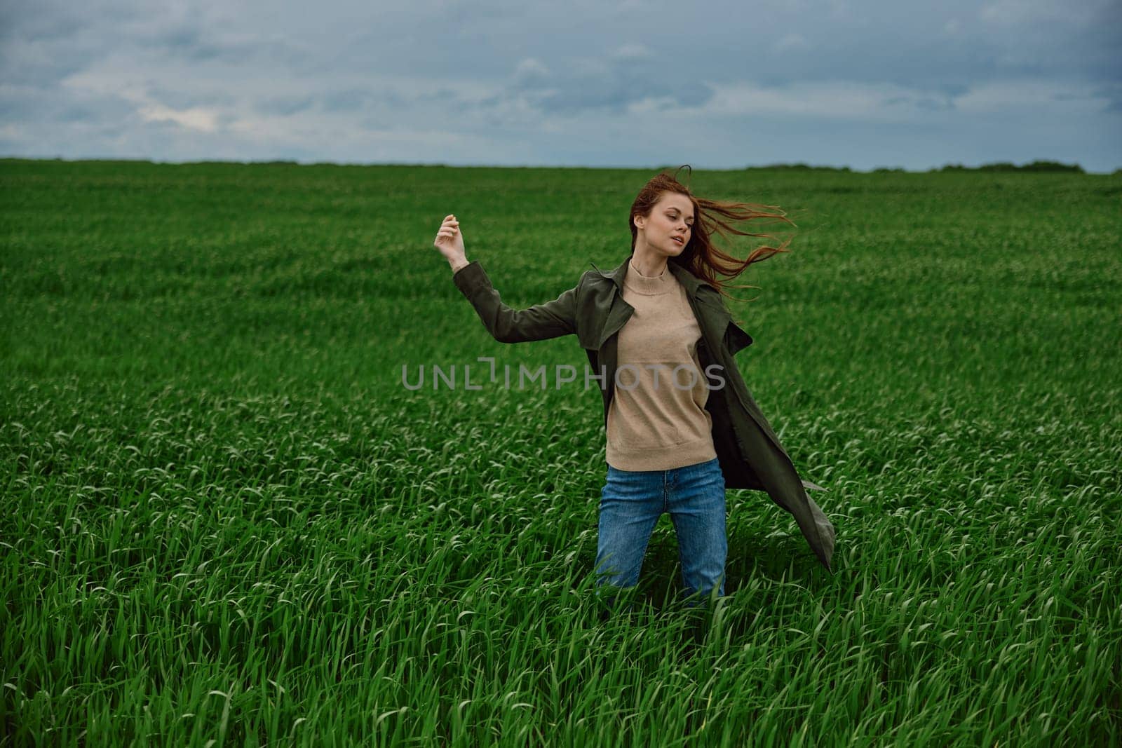 a woman stands in a field in cloudy weather and strong wind facing the camera with her hand raised up. High quality photo