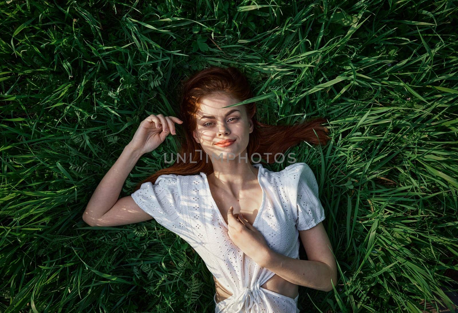 an elegant woman in a light dress lies in the grass and enjoys life by Vichizh