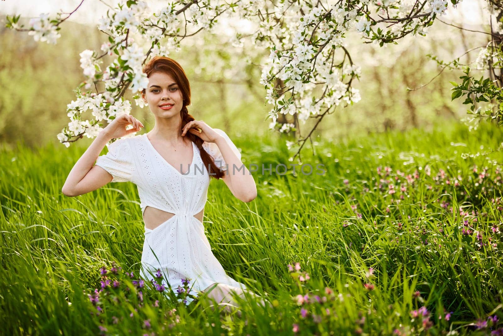 Beautiful woman in a blooming spring garden in a light dress smiling looking at the camera. High quality photo