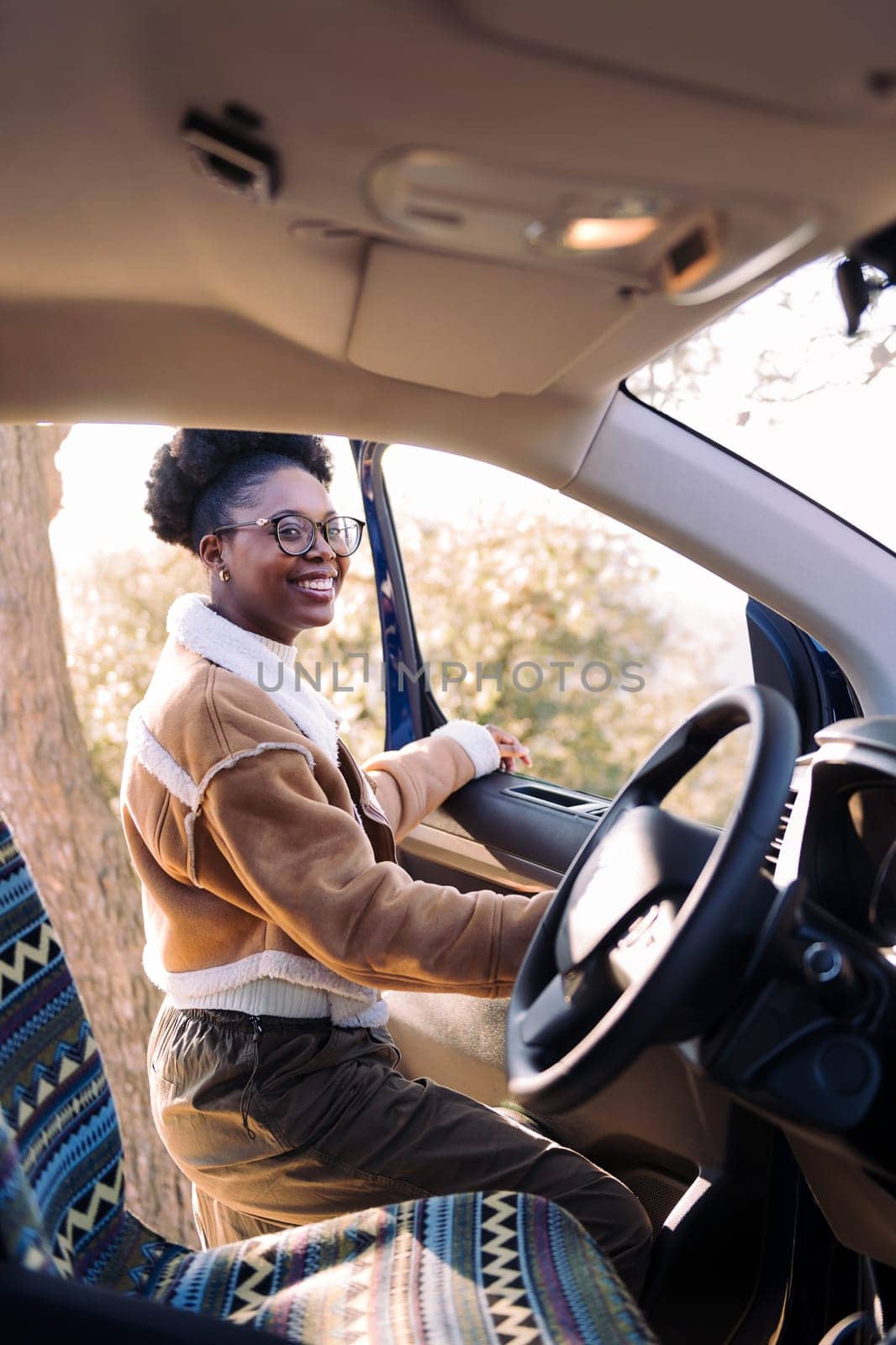 smiling young black woman in a nomadic journey standing by the camper van, concept of freedom and wanderlust