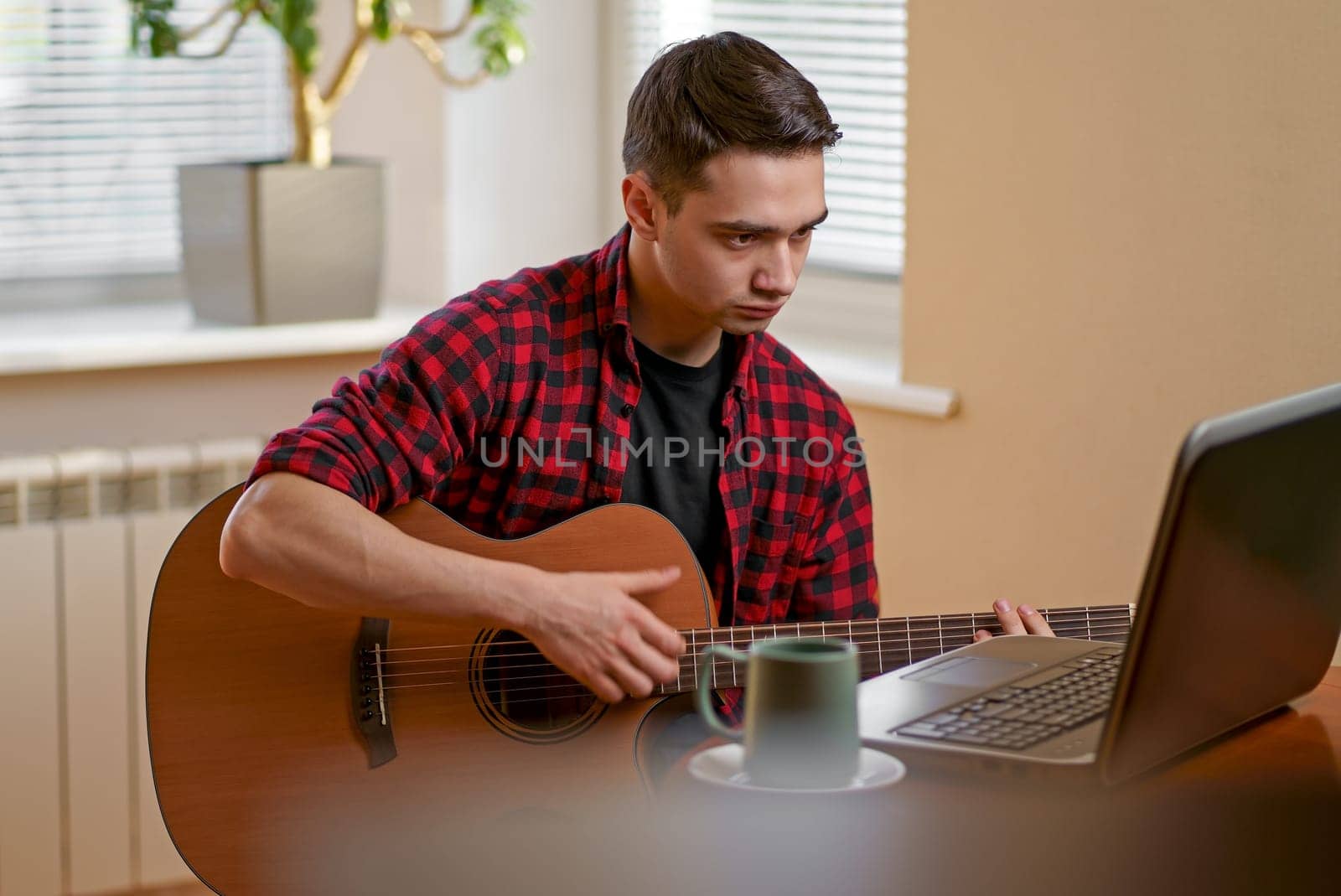 Relaxed man playing the guitar at home and using a laptop