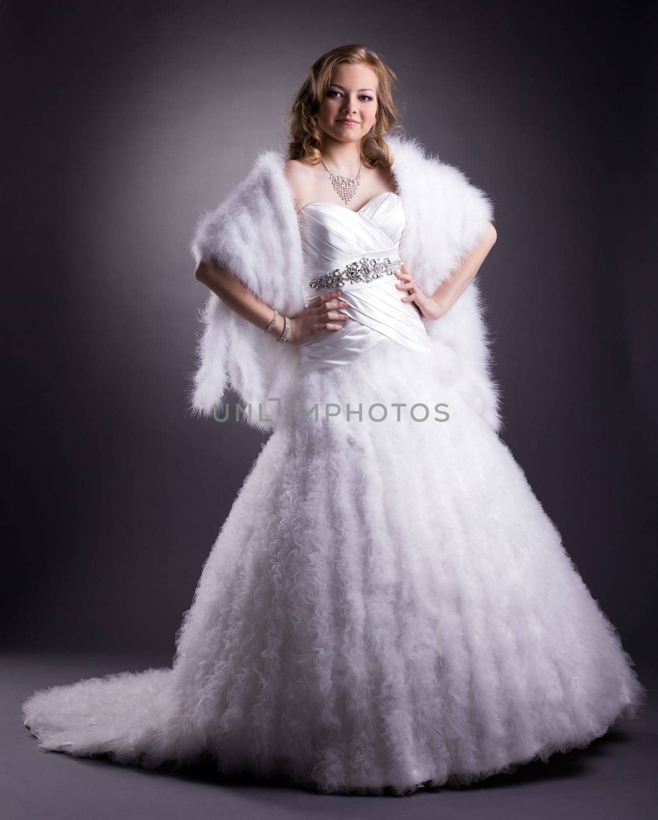 Pretty woman posing in luxurious wedding dress on gray background