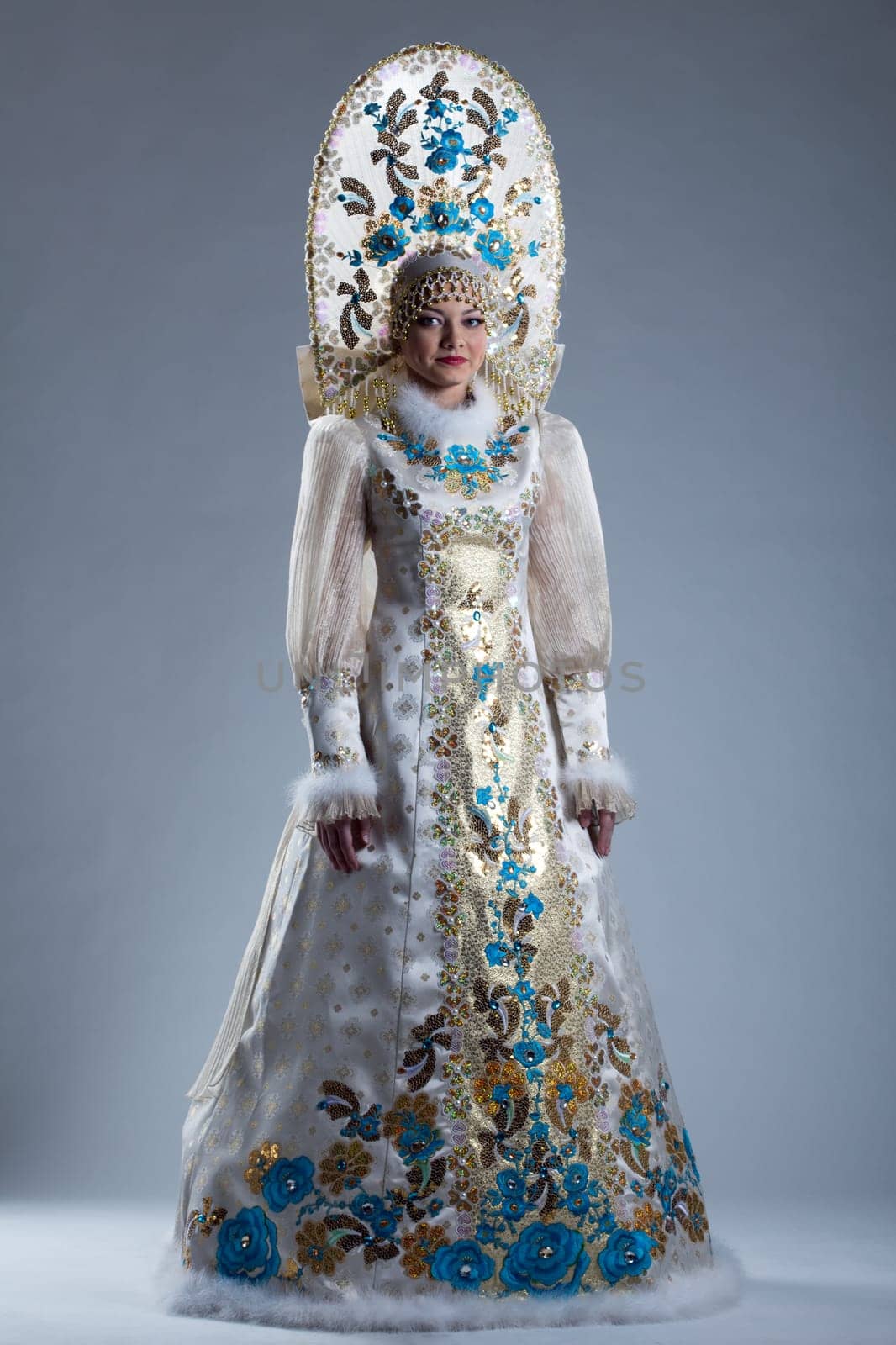 Pretty young girl in Russian costume and kokoshnik posing on blue background