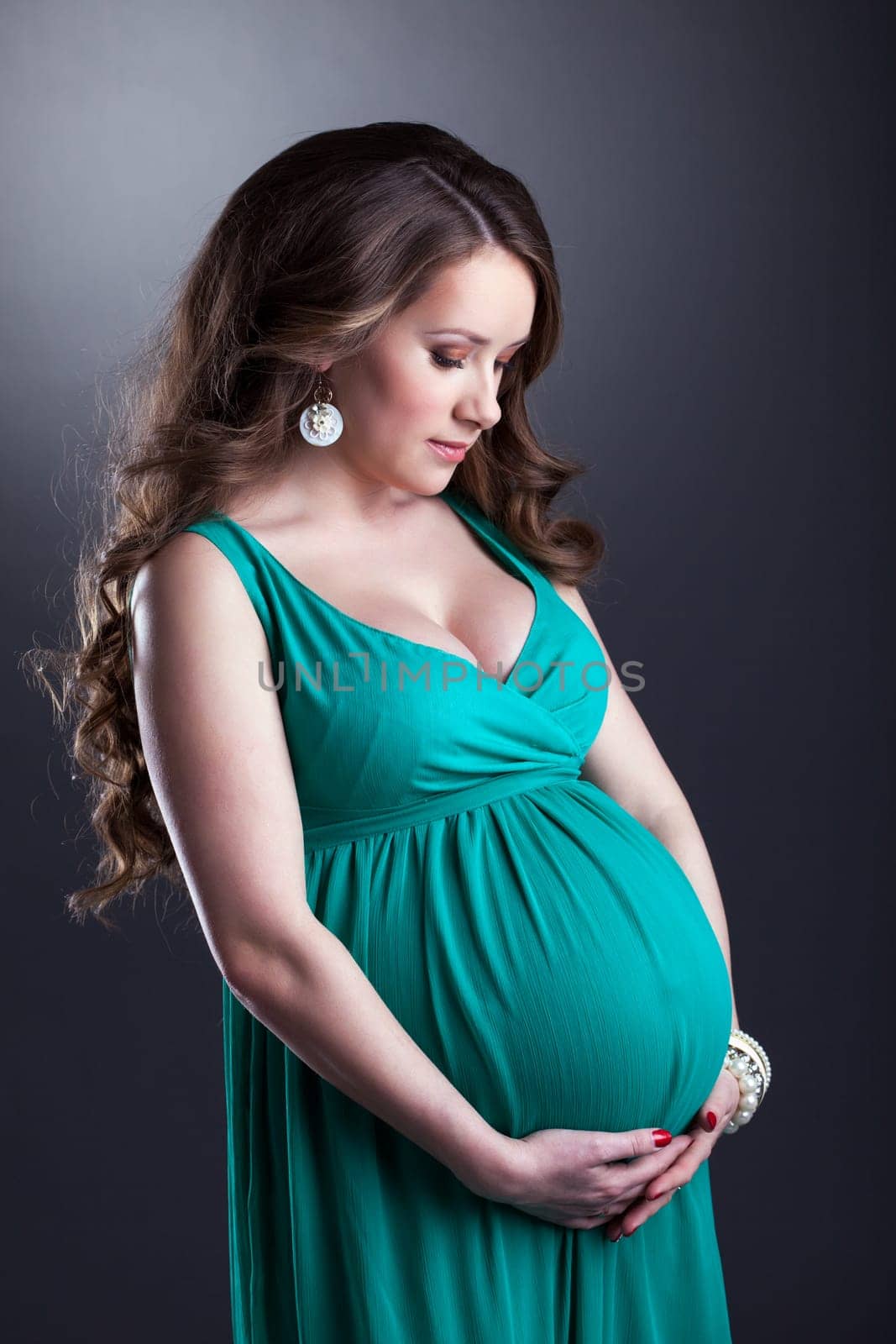 Pretty pregnant woman caressing her belly, on gray background