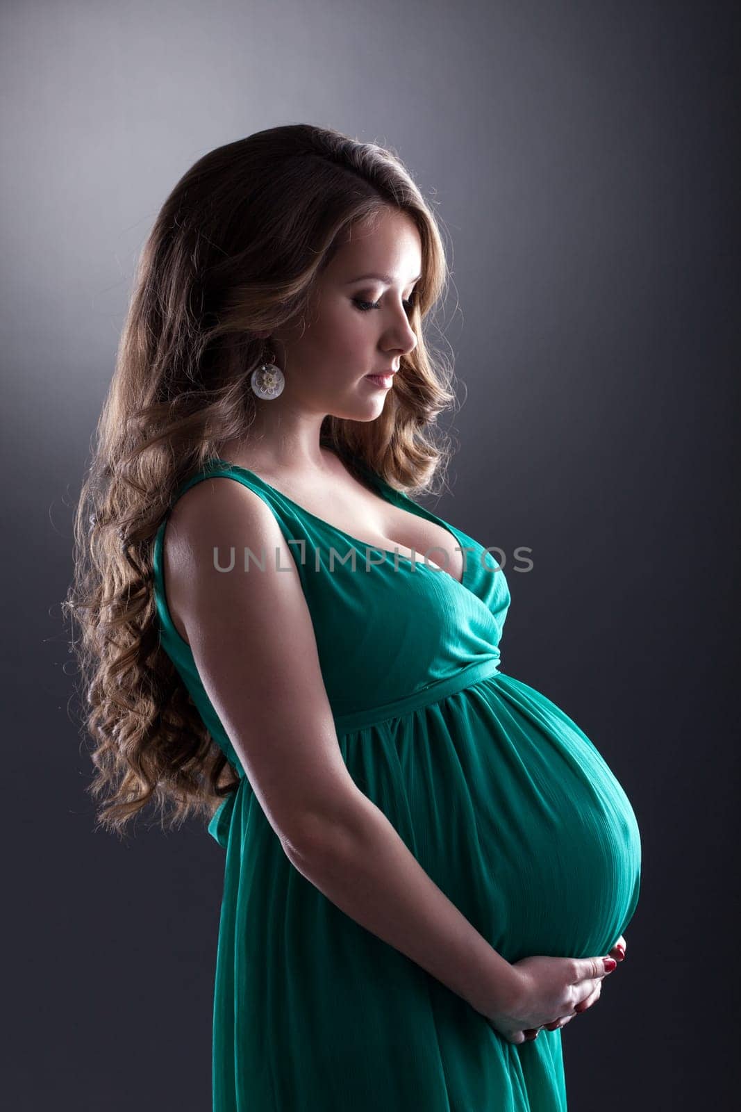 Young expectant woman caressing her belly, on gray background