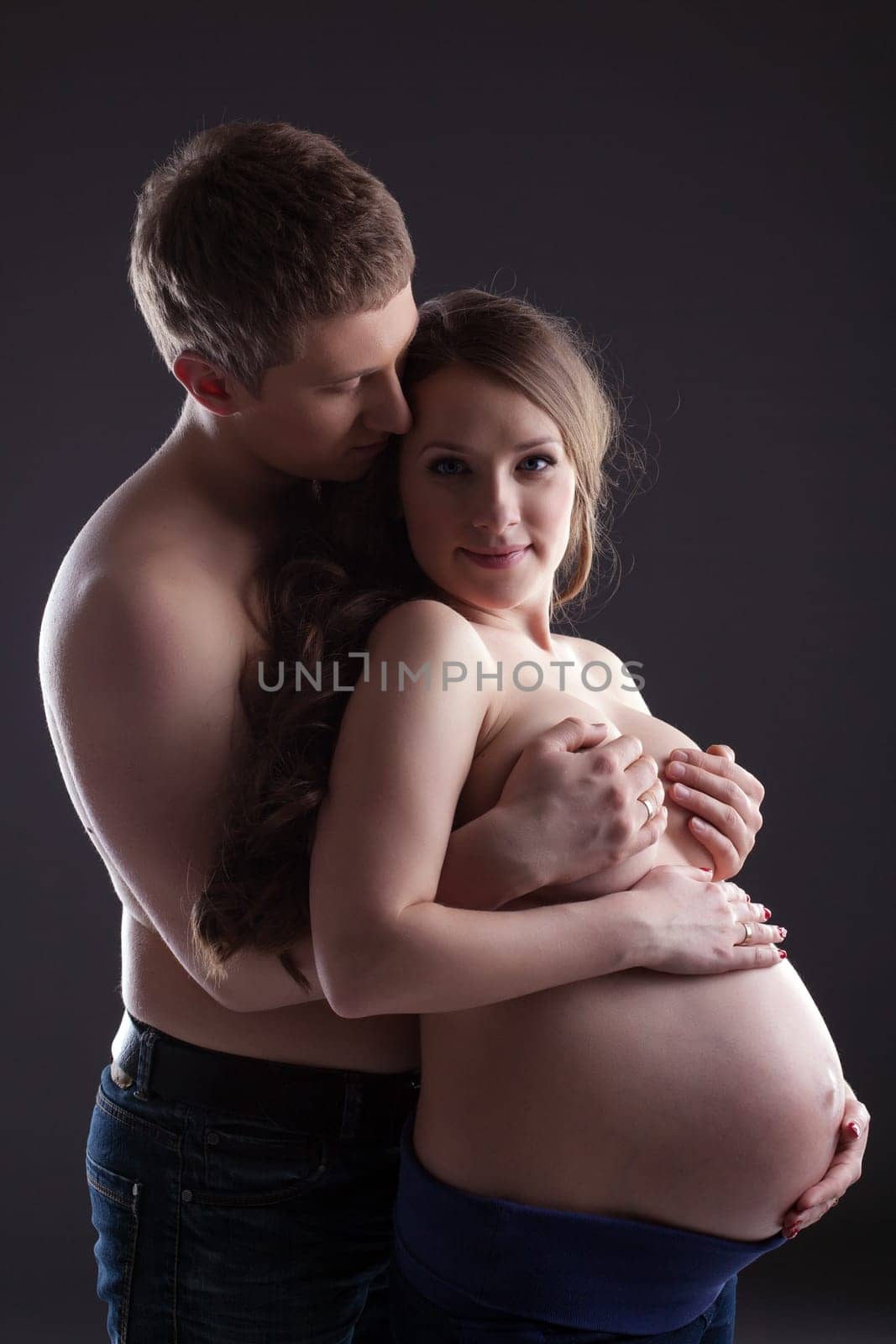 Lovely pregnant woman and man in studio, on gray background