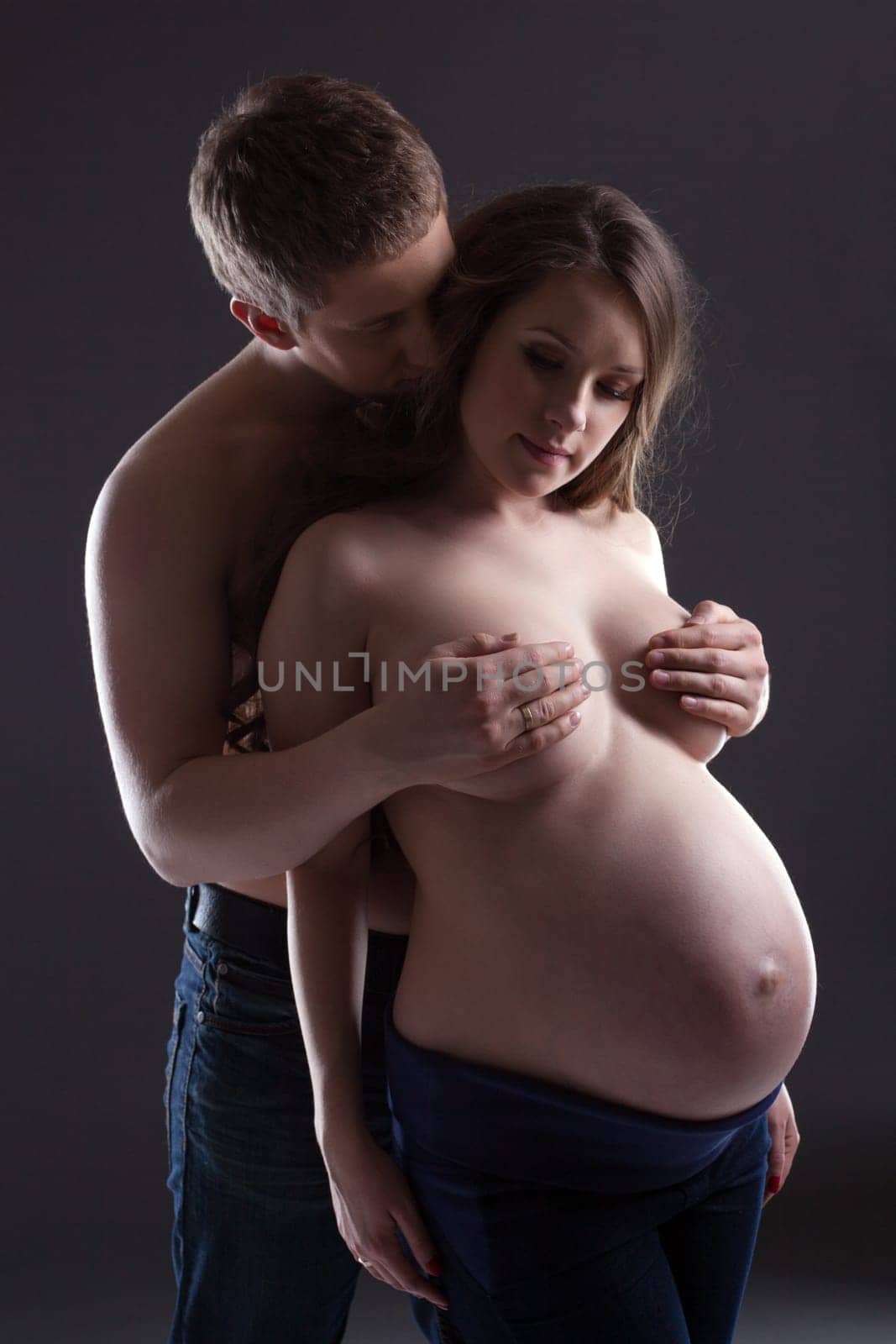 Young man hugging pretty pregnant woman, on gray background