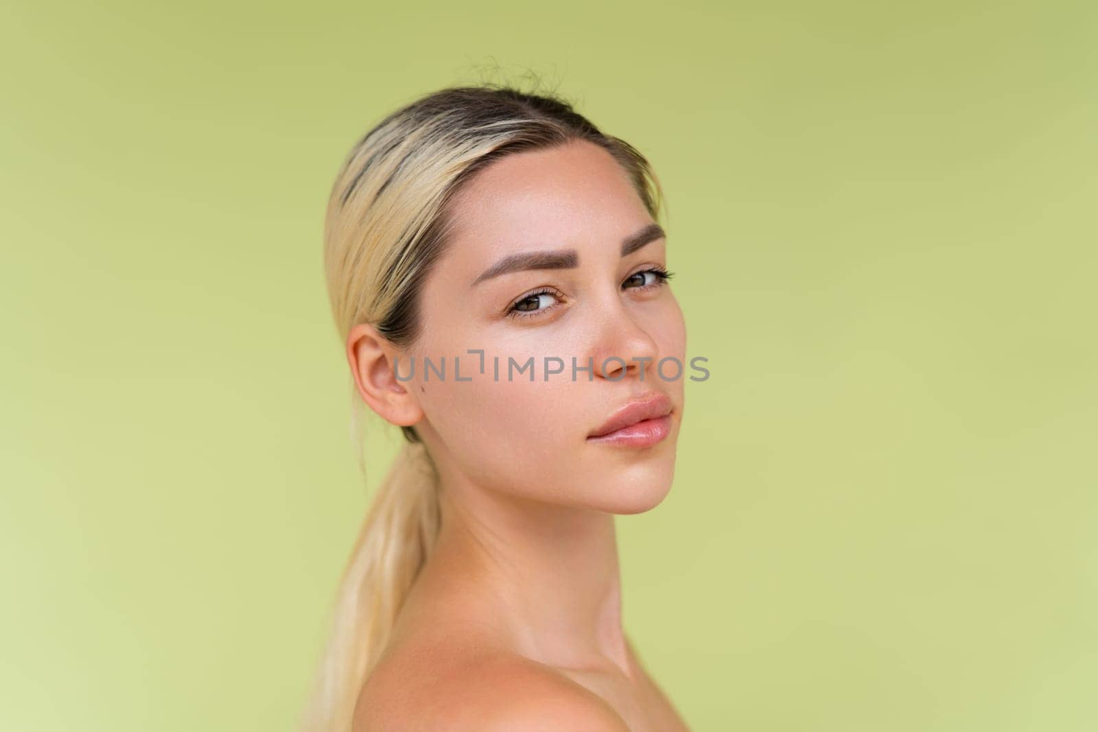 Beauty portrait of young topless woman with bare shoulders on green background with perfect skin and natural makeup