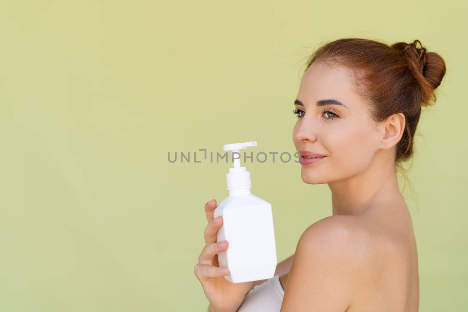 Beauty portrait of young topless red hair woman with bare shoulders on green background with perfect skin holding bottle of shampoo, body lotion by kroshka_nastya