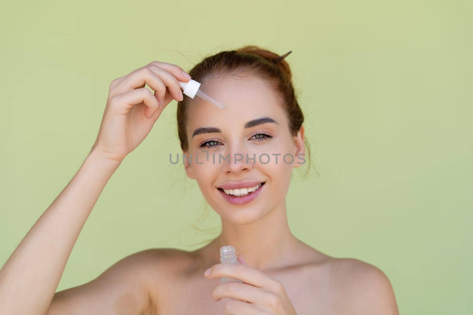 Beauty portrait of young topless red hair woman with bare shoulders on green background with perfect skin holds serum for youth and skin hydration