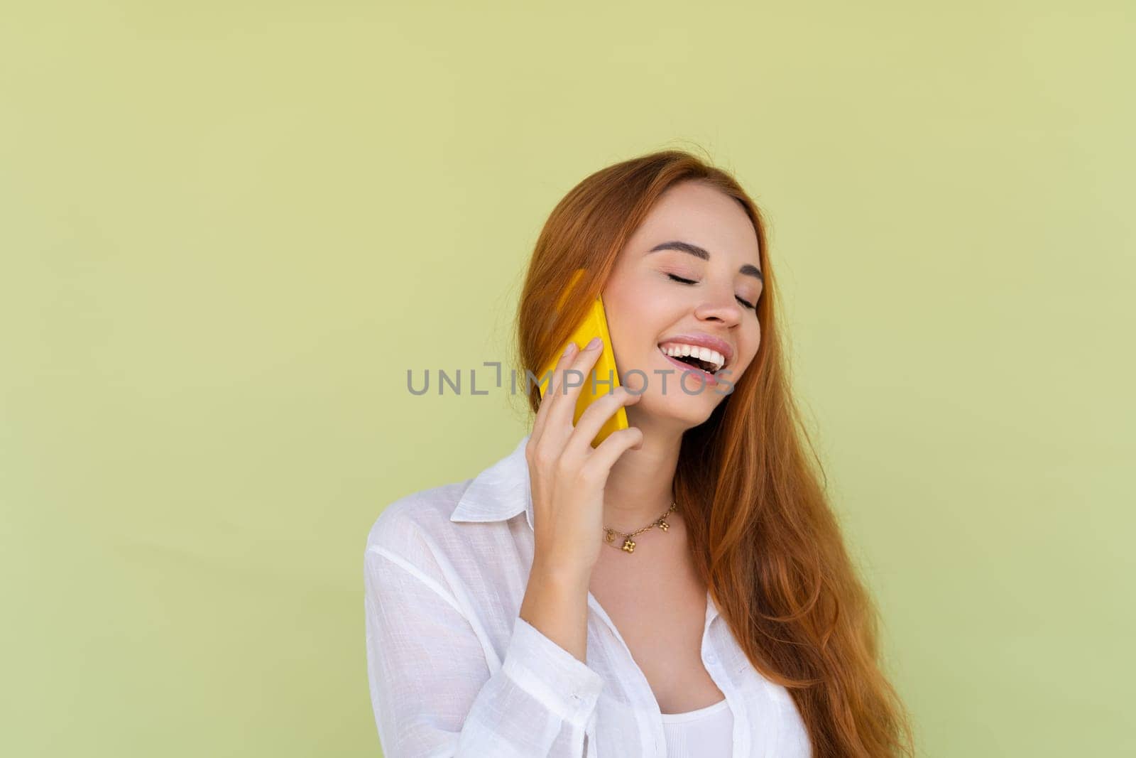 Beautiful red hair woman in casual shirt on green background talk on mobile phone smile and laugh by kroshka_nastya
