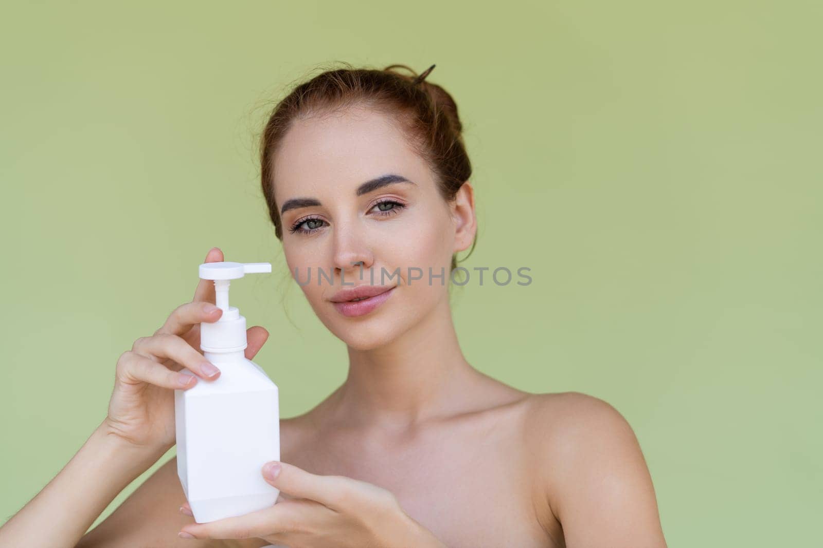 Beauty portrait of young topless red hair woman with bare shoulders on green background with perfect skin holding bottle of shampoo, body lotion by kroshka_nastya