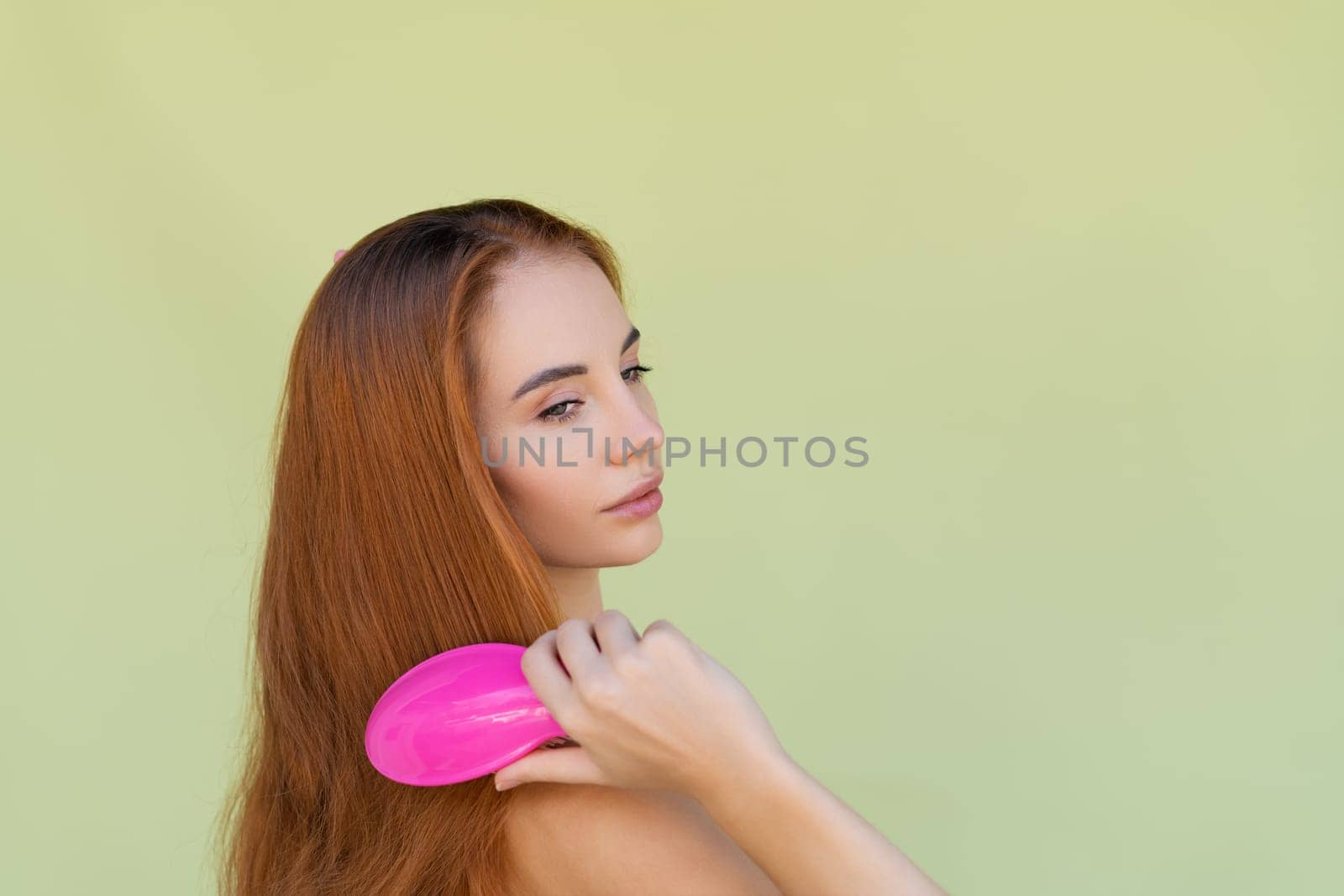 Beauty portrait of young topless red hair woman with bare shoulders on green background brush long strong shiny hair