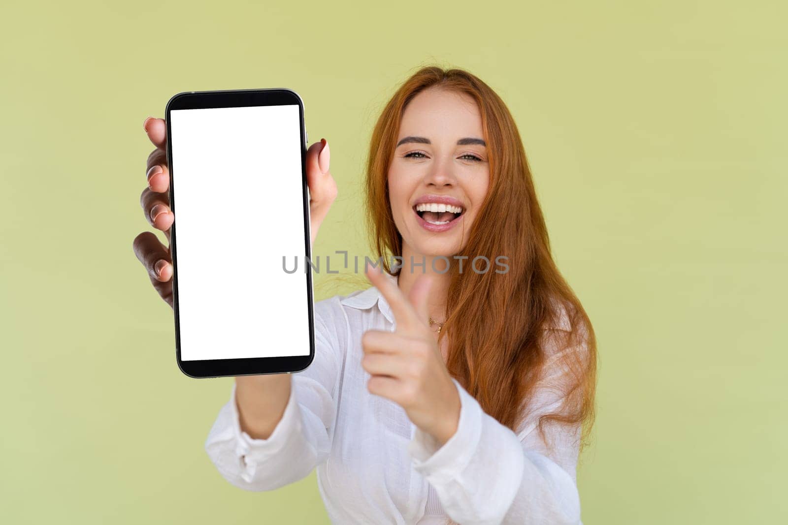 Beautiful red hair woman in casual shirt on green background holds a phone with a blank white screen by kroshka_nastya