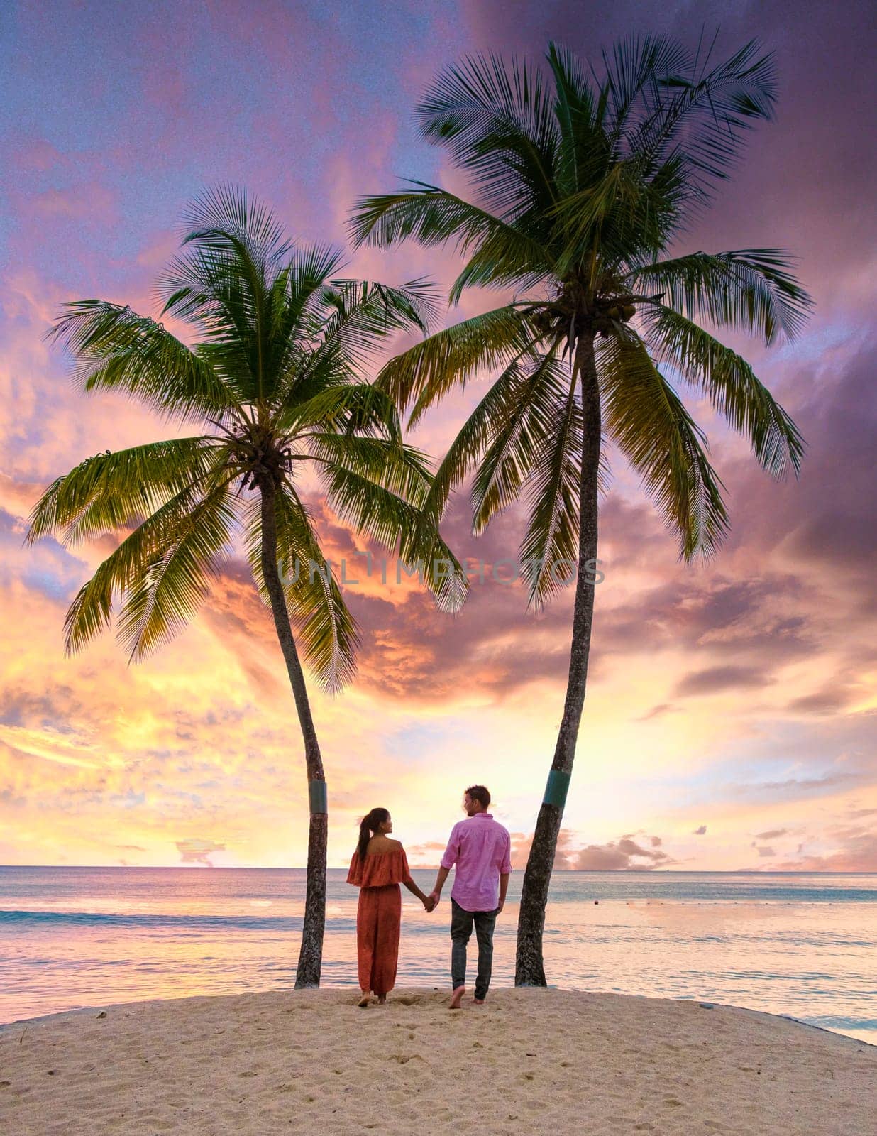couple on the beach with palm trees watching the sunset at the tropical beach of Saint Lucia or St Lucia Caribbean. men and women on vacation in St Lucia a tropical island with palm trees