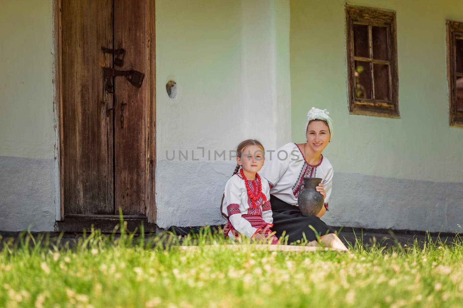 mother and daughter in traditional Ukrainian clothes are sitting near the house