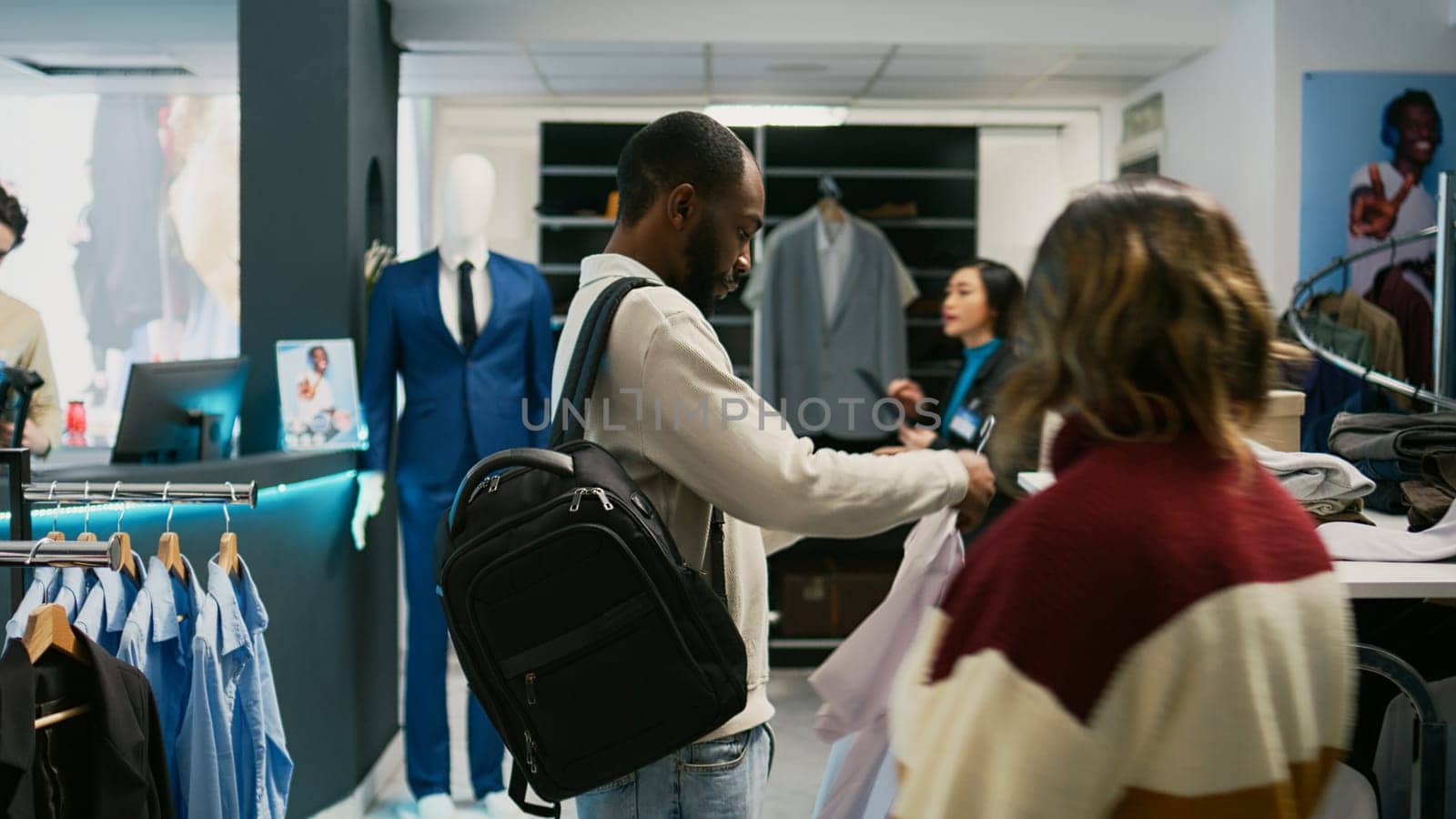 Retail customer examining new shirts collection to buy formal wear at shopping mall, looking at clothing store merchandise. Young adult shopping for modern clothes in fashion boutique.