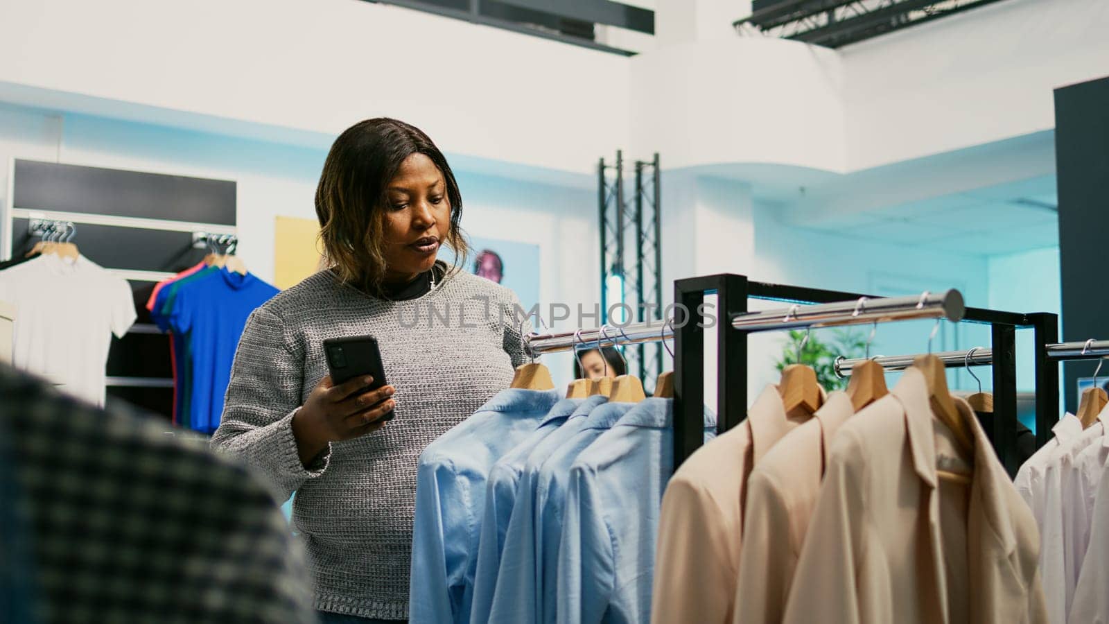 Female customer checking website stock at store, using mobile phone to look at modern online merchandise. Young shopaholic adult examining new fashion trends, commercial activity.