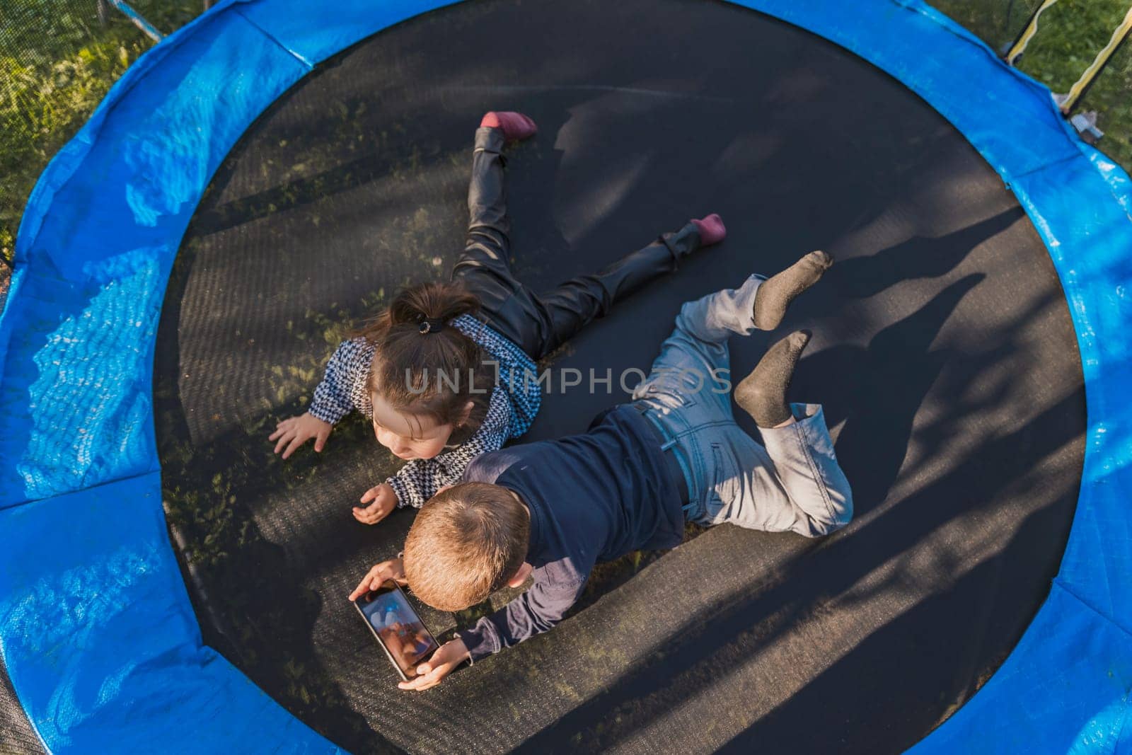 children look at the phone while lying on a trampoline by zokov