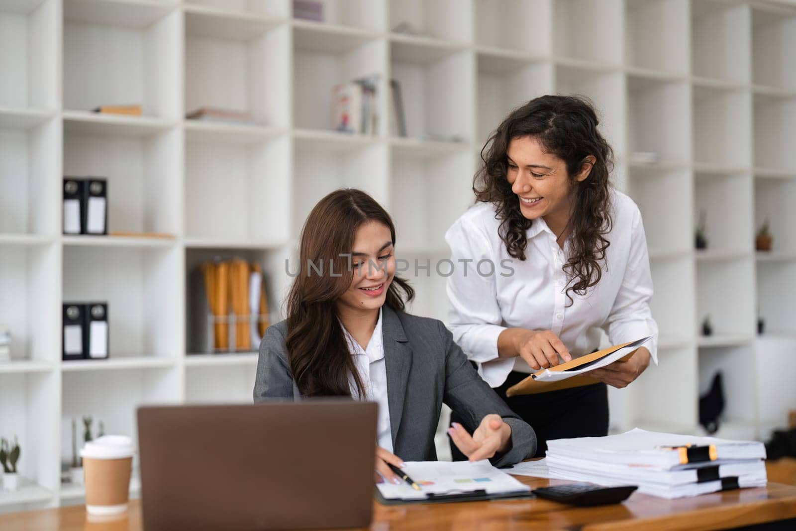 Two diverse female smiling while working together at a boardroom table during a meeting in a modern office.