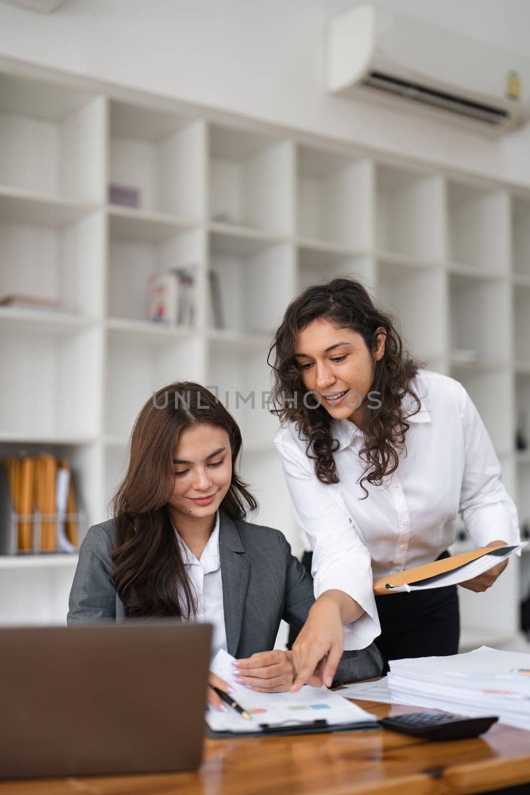 Two diverse female smiling while working together at a boardroom table during a meeting in a modern office by nateemee