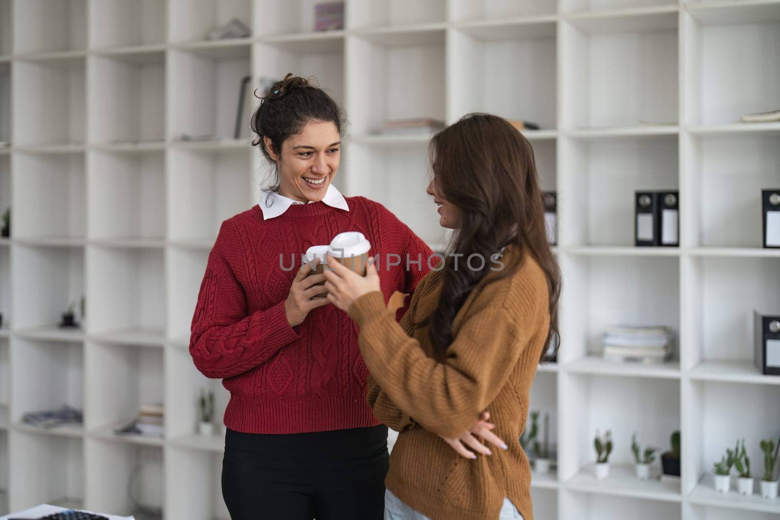 Two diverse female smiling while working together at a boardroom table during a meeting in a modern office.