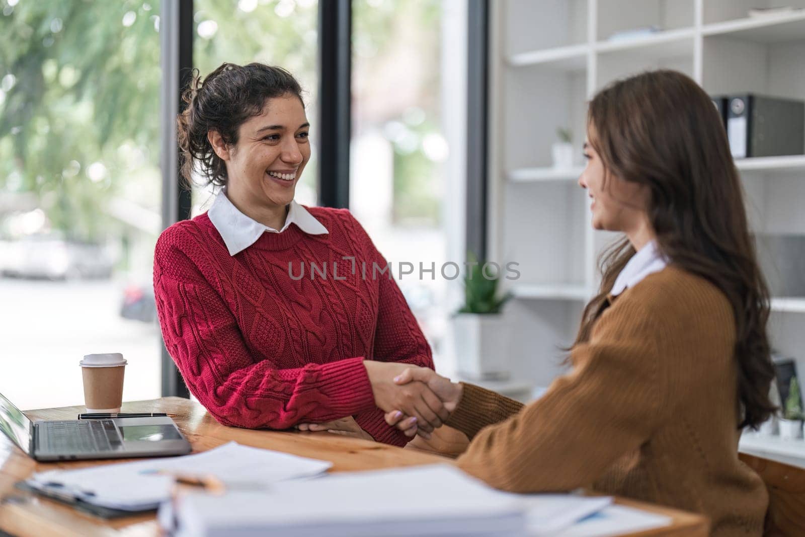 Two diversity women shake hands confidently professional investor working with new startup project at an office meeting. by nateemee